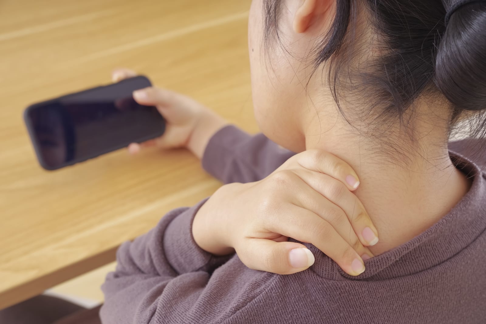 スマートフォンを見ながら首の後ろを押さえる女性