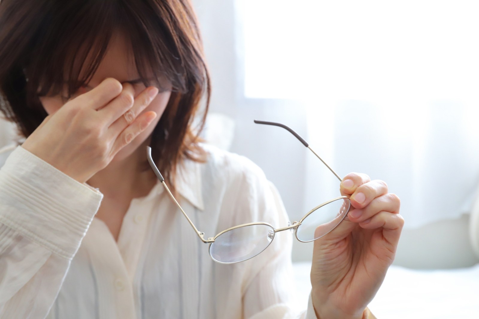 パソコン作業で眼精疲労を感じ目を押さえる女性